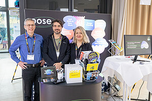 Drei Personen stehen vor einem Stand mit einem Computer.