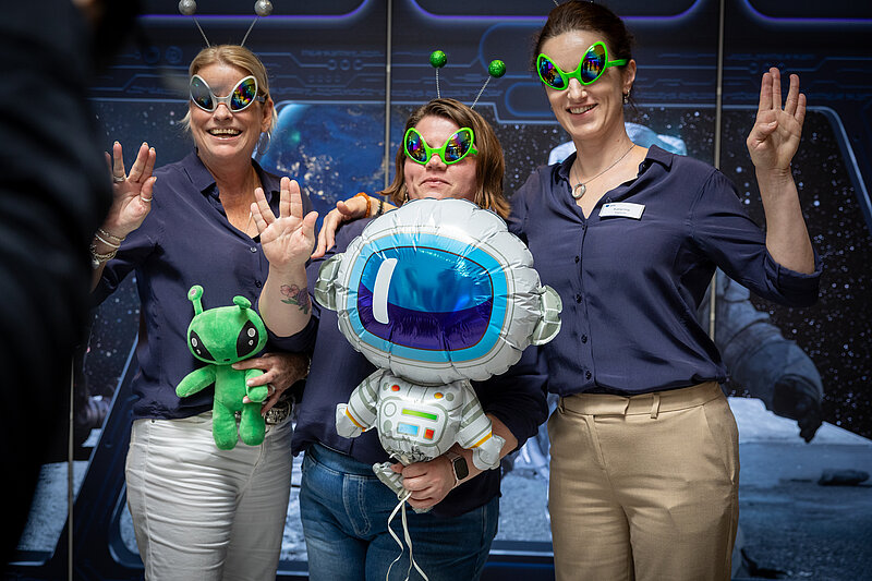 Three women wearing glasses stand together and smile at the camera.