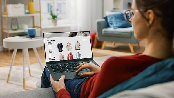 Frau sitzt auf dem Sofa und nutzt einen Laptop, um online einzukaufen.