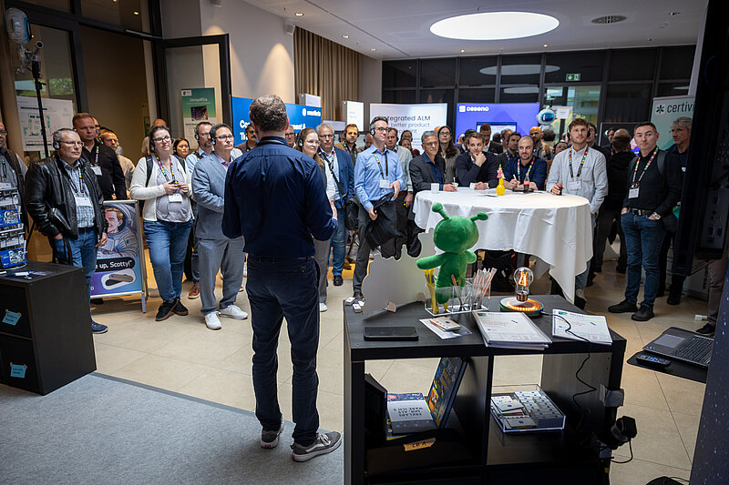 A group of people are standing around a table while a man gives a presentation.
