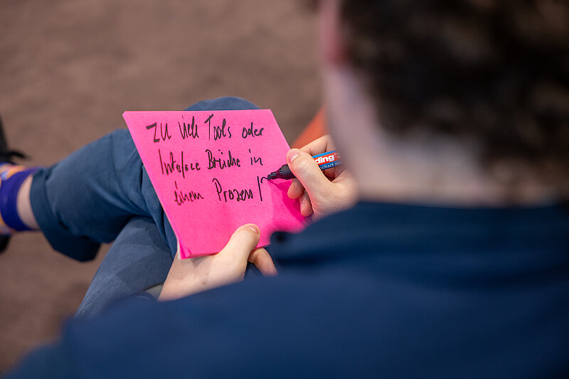 A person is sitting on the floor holding a pink piece of paper in their hand.