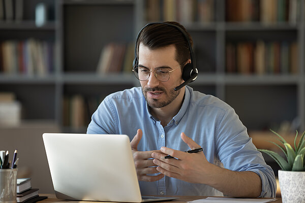 A man wearing headphones sits at a desk in front of a laptop.