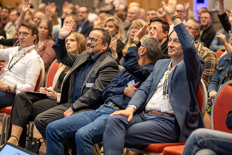 A group of people are sitting in chairs and raising their hands.