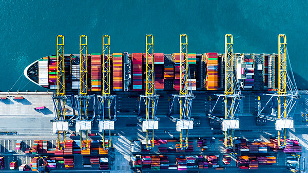 Aerial view of a container ship docked at a port, surrounded by other ships and port facilities.