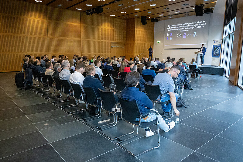A large group of people are sitting in chairs in a room and listening attentively.
