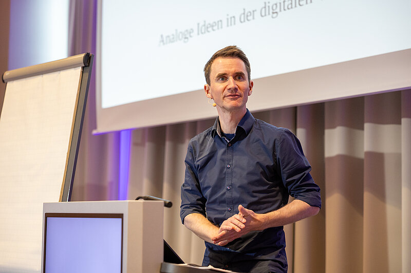A man stands at a podium in front of a screen and speaks to an audience.