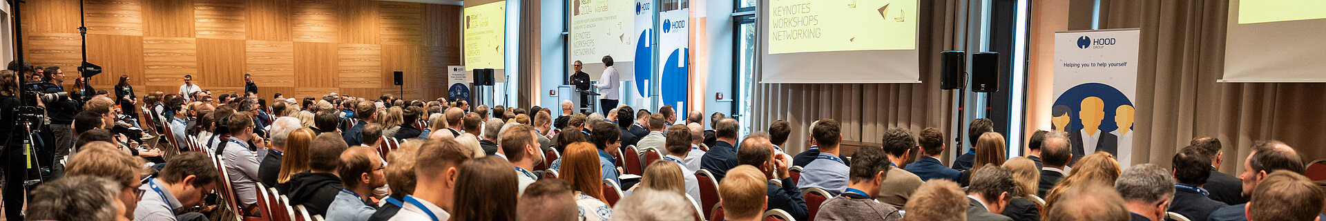 Eine große Gruppe von Menschen sitzt in einem Konferenzraum auf Stühlen.