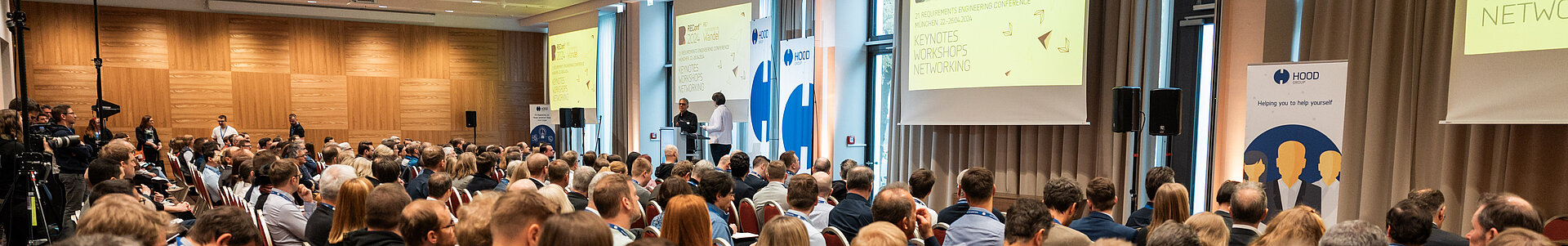 Eine große Gruppe von Menschen sitzt in einem Konferenzraum auf Stühlen.