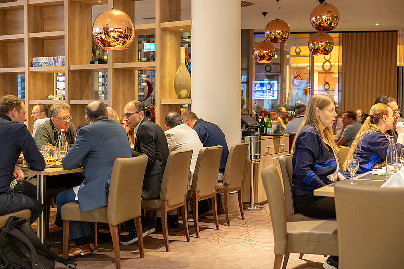 People are sitting at tables in a restaurant, surrounded by bottles of wine.